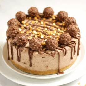 A Ferrero Rocher Cheesecake on a plate from the side, with a biscuit base, thick layer or cream and chocolatey topping.