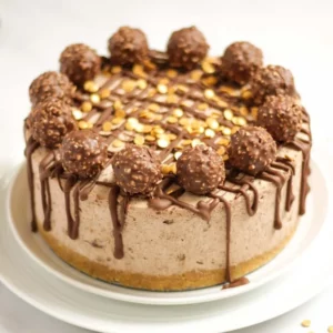 A Ferrero Rocher Cheesecake on a plate from the side, with a biscuit base, thick layer or cream and chocolatey topping.