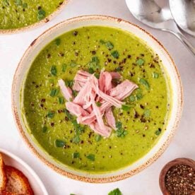 A pan of green Pea and Ham Soup with shredded ham on top, ready to eat.