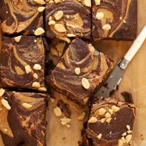 Squares of peanut butter brownies cut into squares with a knife on a chopping board.
