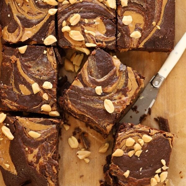 Squares of peanut butter brownies cut into squares with a knife on a chopping board.