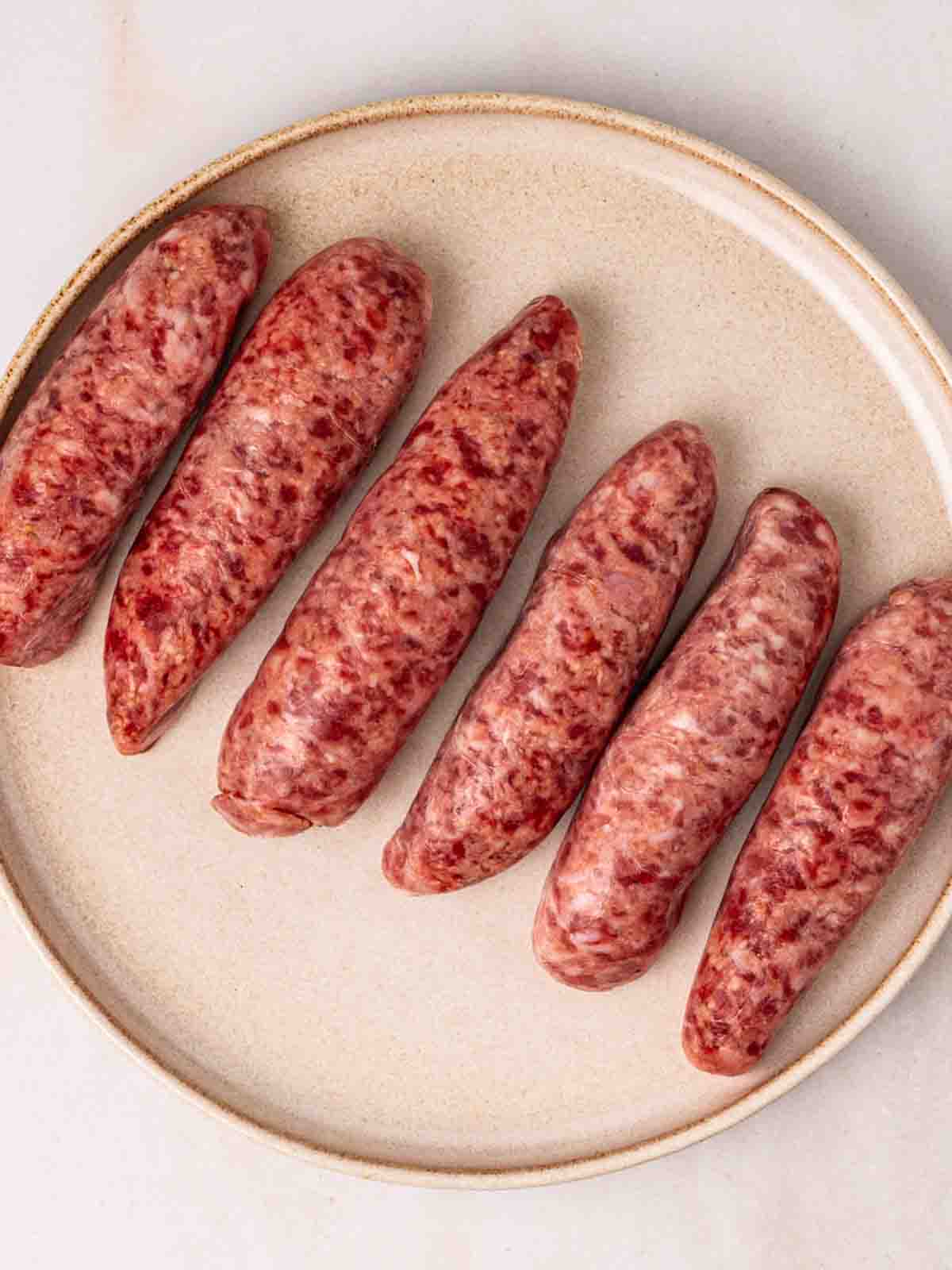 Six raw sausages on a plate, waiting to be air fried.