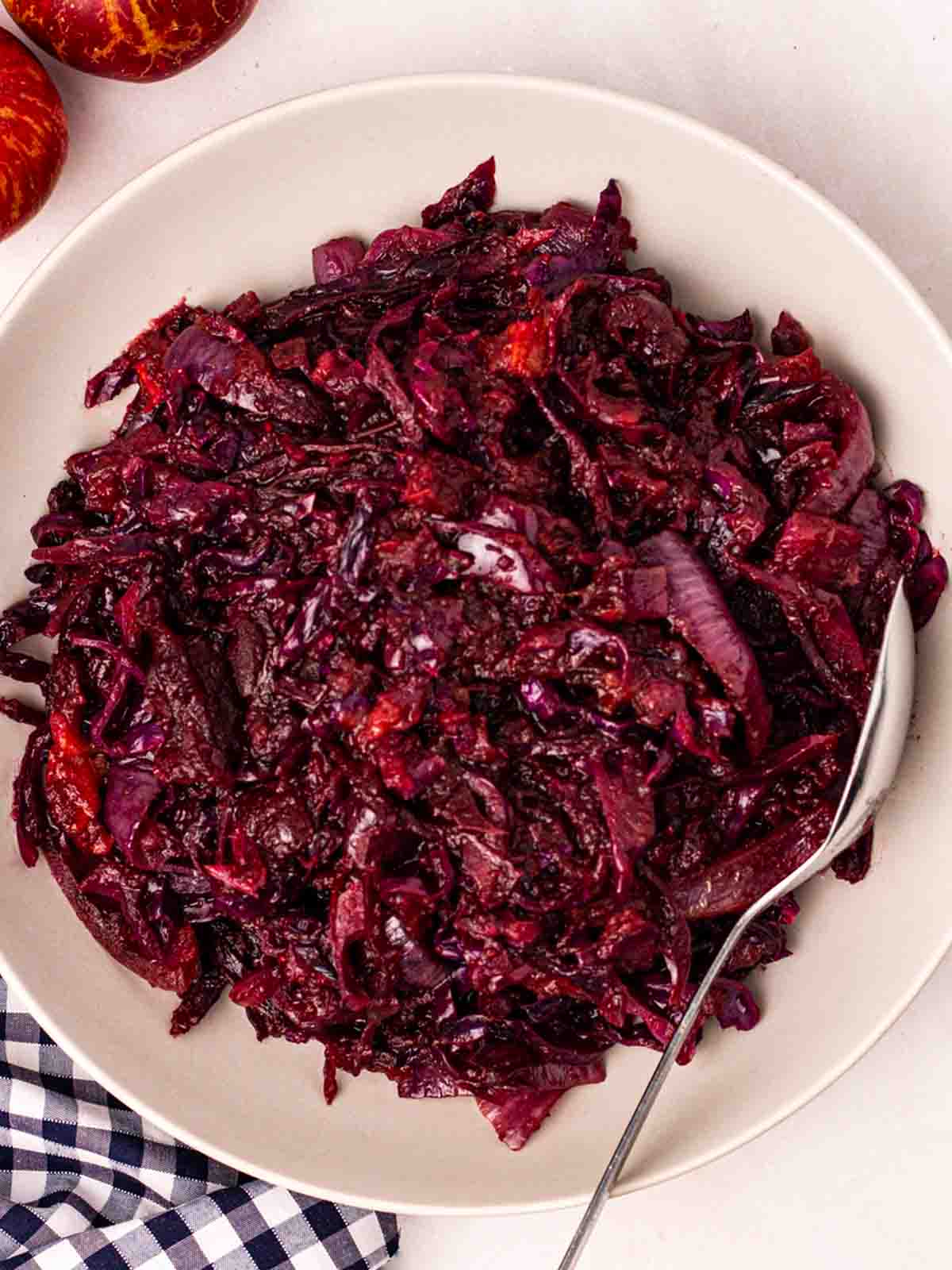 A bowl of braised red cabbage with a spoon in on a white table cloth.