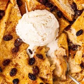 A close up of bread and butter pudding with raisins and a dollop of ice cream.