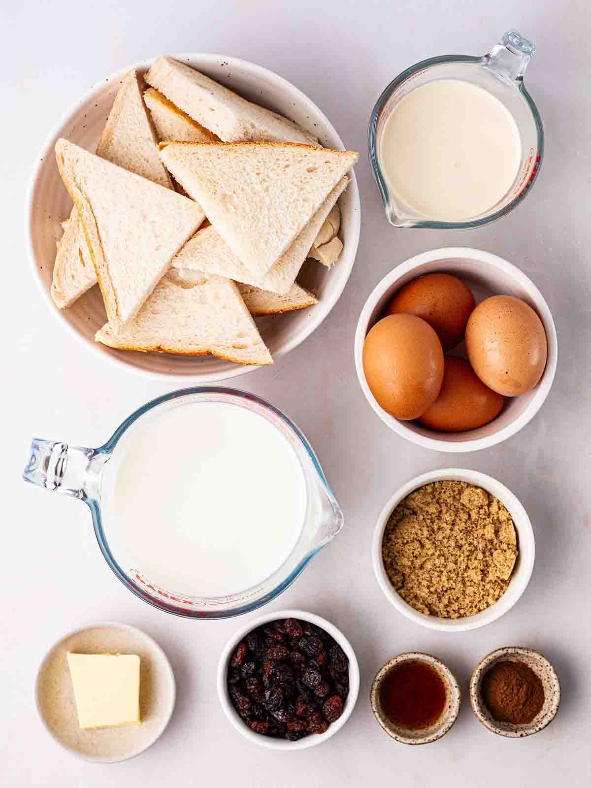 The ingredients to make bread and butter pudding laid out on a white counter.