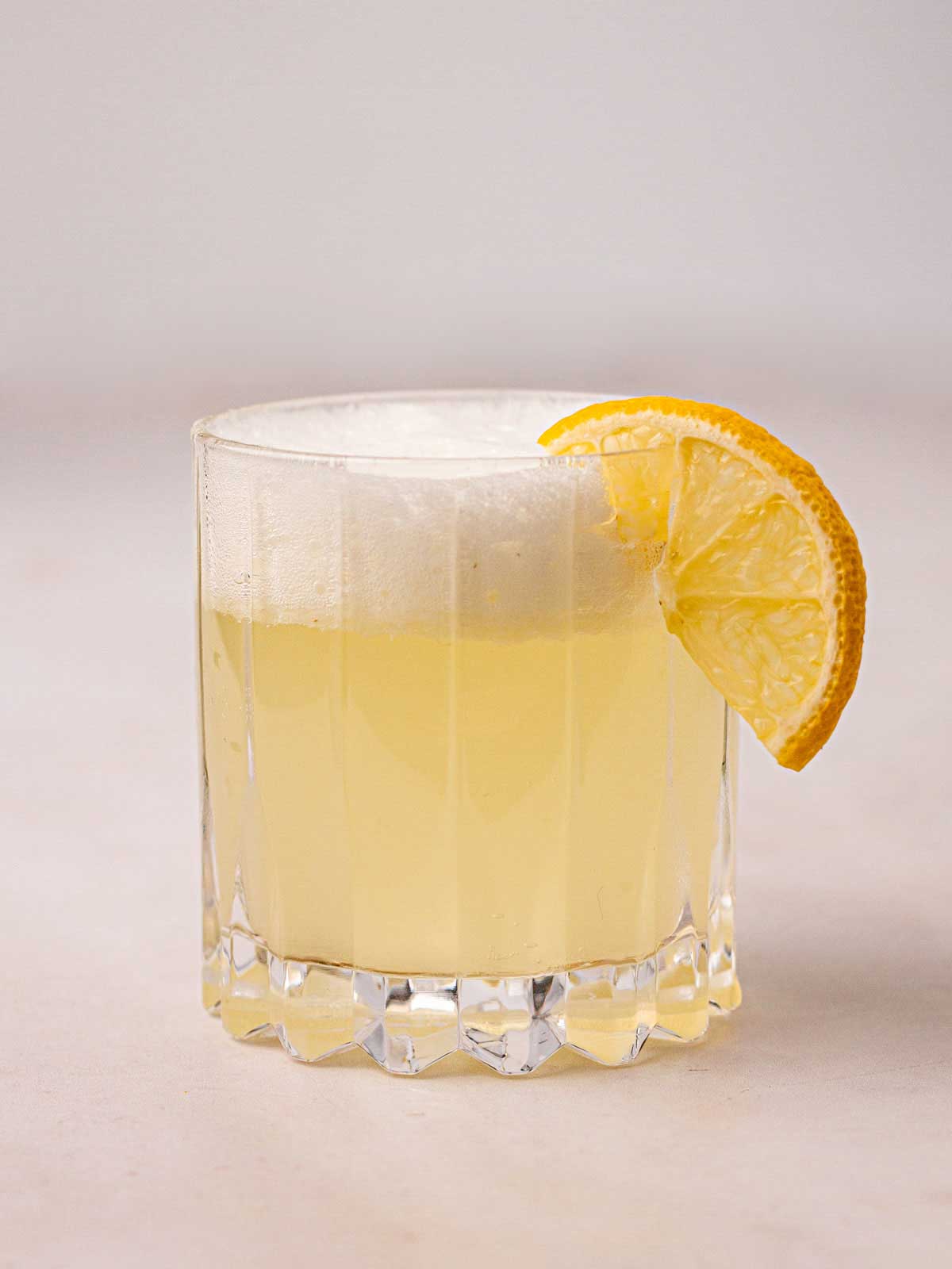 A frothy Gin Fizz Cocktail in a glass with a slice of lemon in the side.