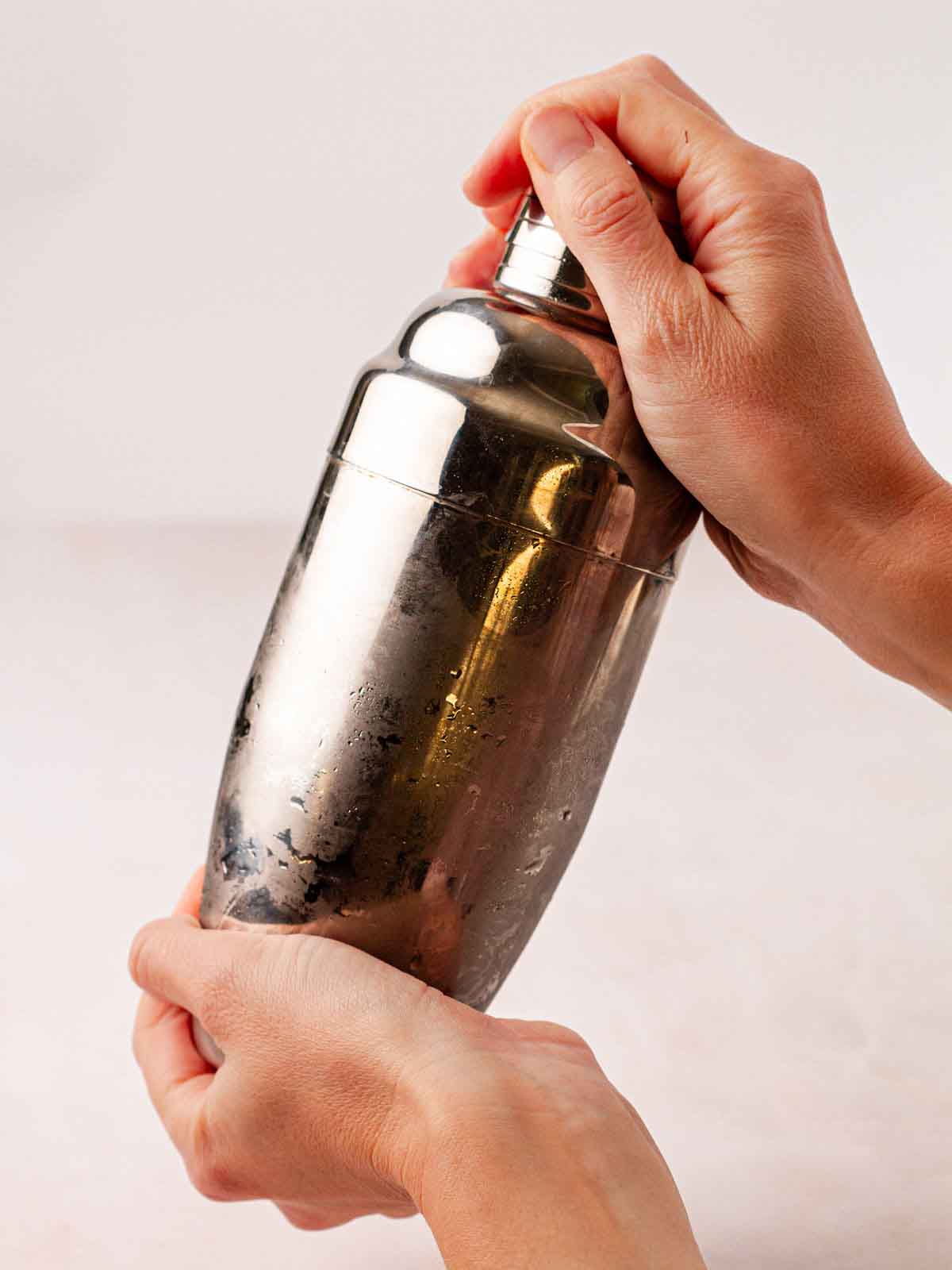 Two hands holding a cocktail shaker, in the act of mixing a Gin Fizz.