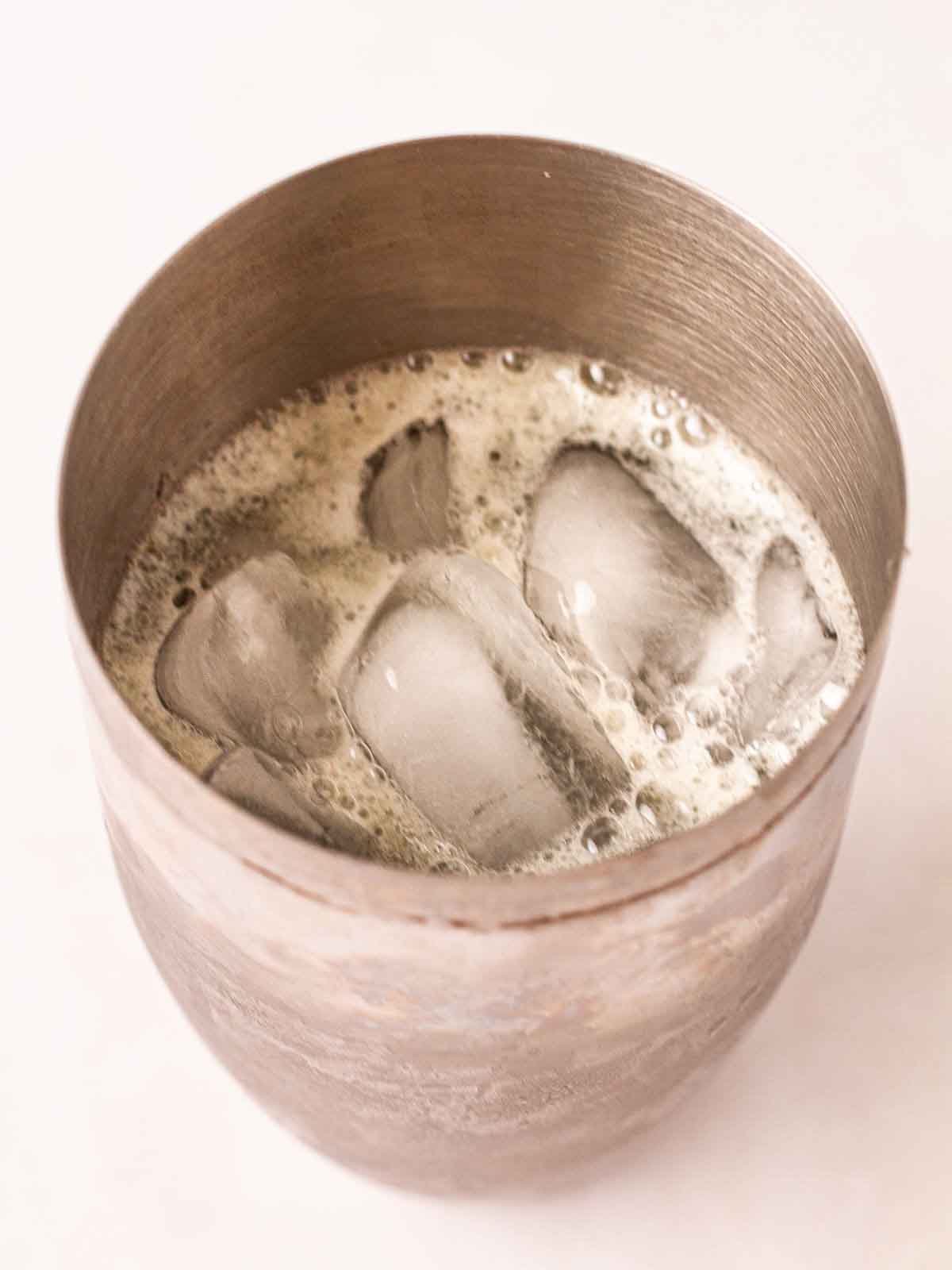 A cocktail shaker filled with ice and gin and egg white for step 2 in the recipe for Gin Fizz.