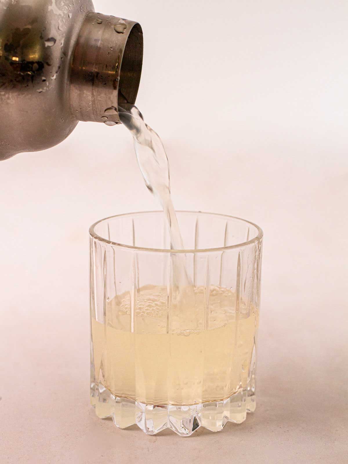 A cocktail mixer with a Gin Fizz Cocktail pouring out into a glass for step 4 in a gin cocktail recipe.