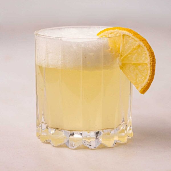 A glass filled with Gin Fizz, with frothy egg white on top and a slice of lemon.