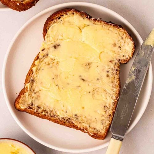 A slice of bread with a thick layer of homemade butter on, with a knife to the side on the plate.