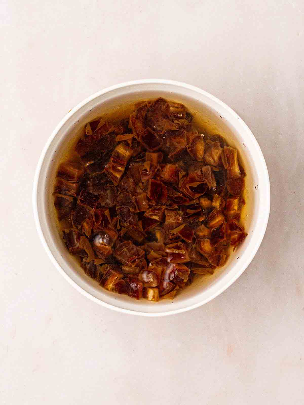 Chopped up dates soaking in a bowl for step 1 in the method for Slow Cooker Sticky Toffee Pudding, step 1.