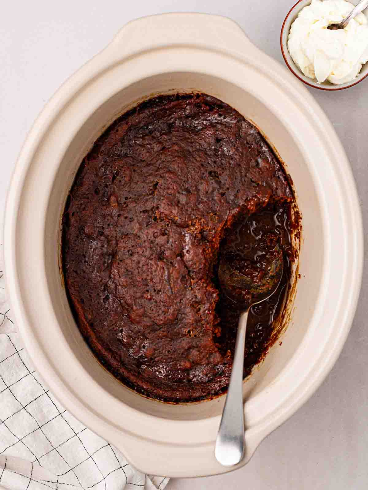 A slow cooker filled with sticky toffee pudding, ready to serve with a spoon.