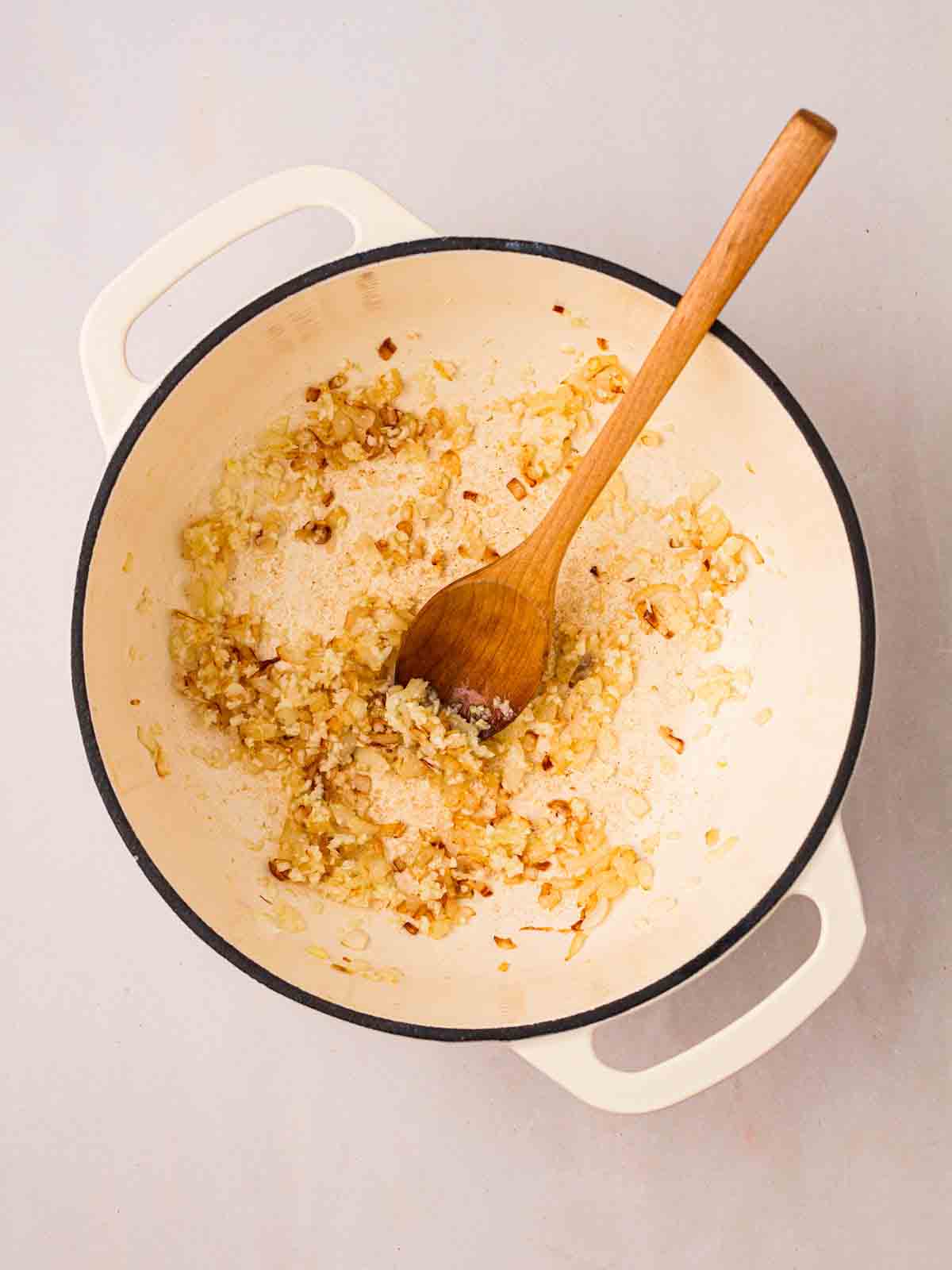 Onions being sautéed in a large pan with a wooden spoon in.
