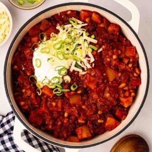 A pan filled with rich Veggie Chilli, with sour cream and spring onions on top.