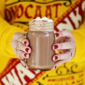 An Advocaat Hot Chocolate being held in two hands withe a yellow jumper in the background.