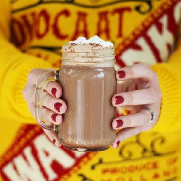 An Advocaat Hot Chocolate being held in two hands withe a yellow jumper in the background.