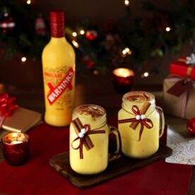 A very festive table with candlelight and two Snowball cocktails, with a bottle of Advocaat in the background.
