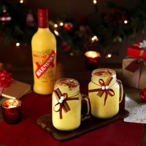 A very festive table with candlelight and two Snowball cocktails, with a bottle of Advocaat in the background.