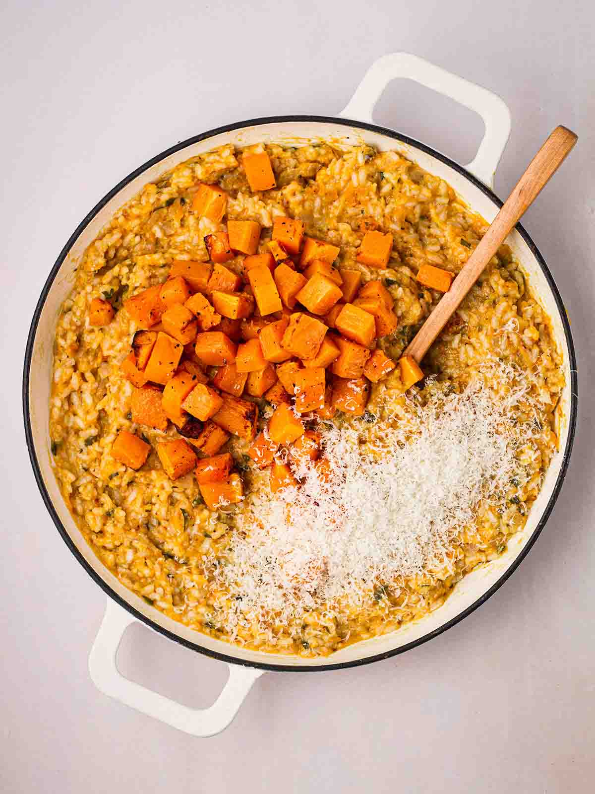 A pan filled with cooked butternut squash risotto, with chunks of the vegetable on top and grated parmesan to stir in.