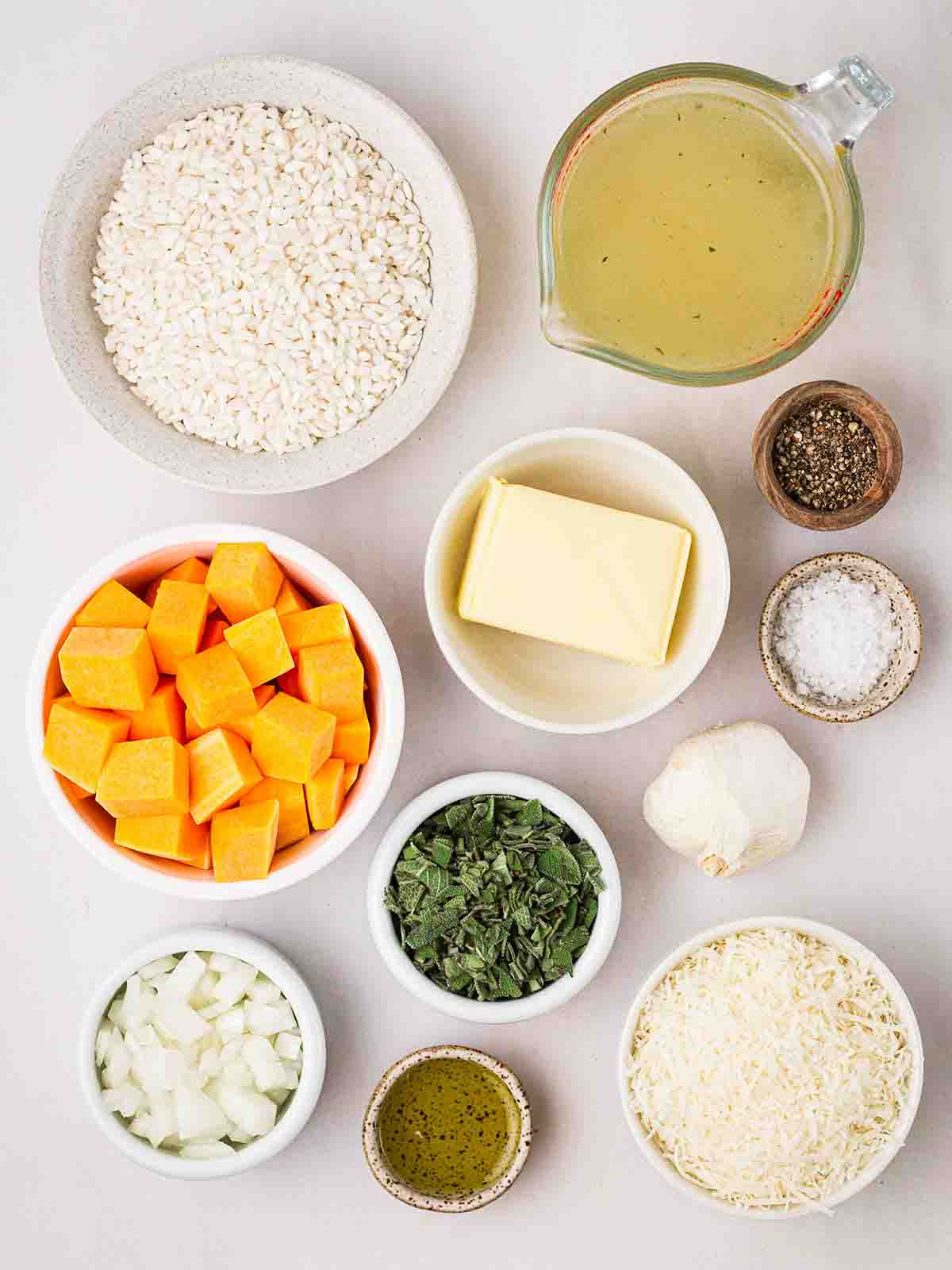The ingredients for a Butternut Squash Risotto laid out in bowls on a white counter.
