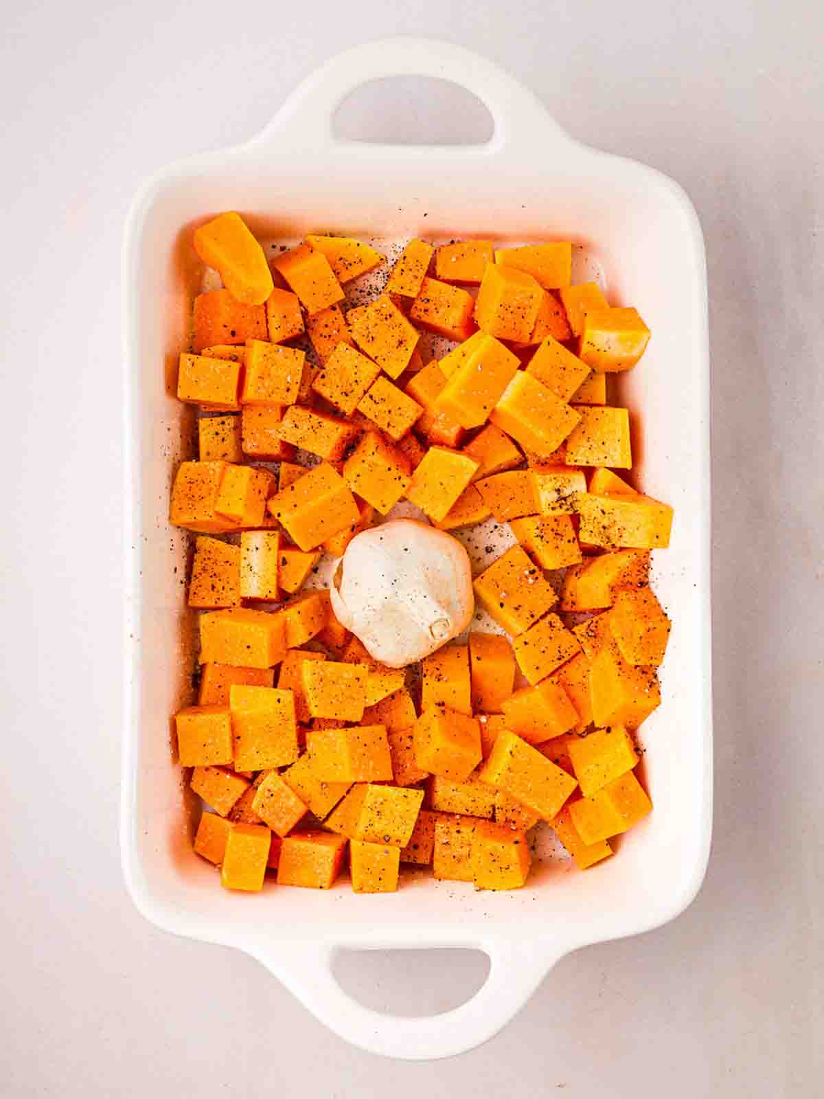 An oven dish with squares of butternut squash in and a bulb of garlic in the middle.