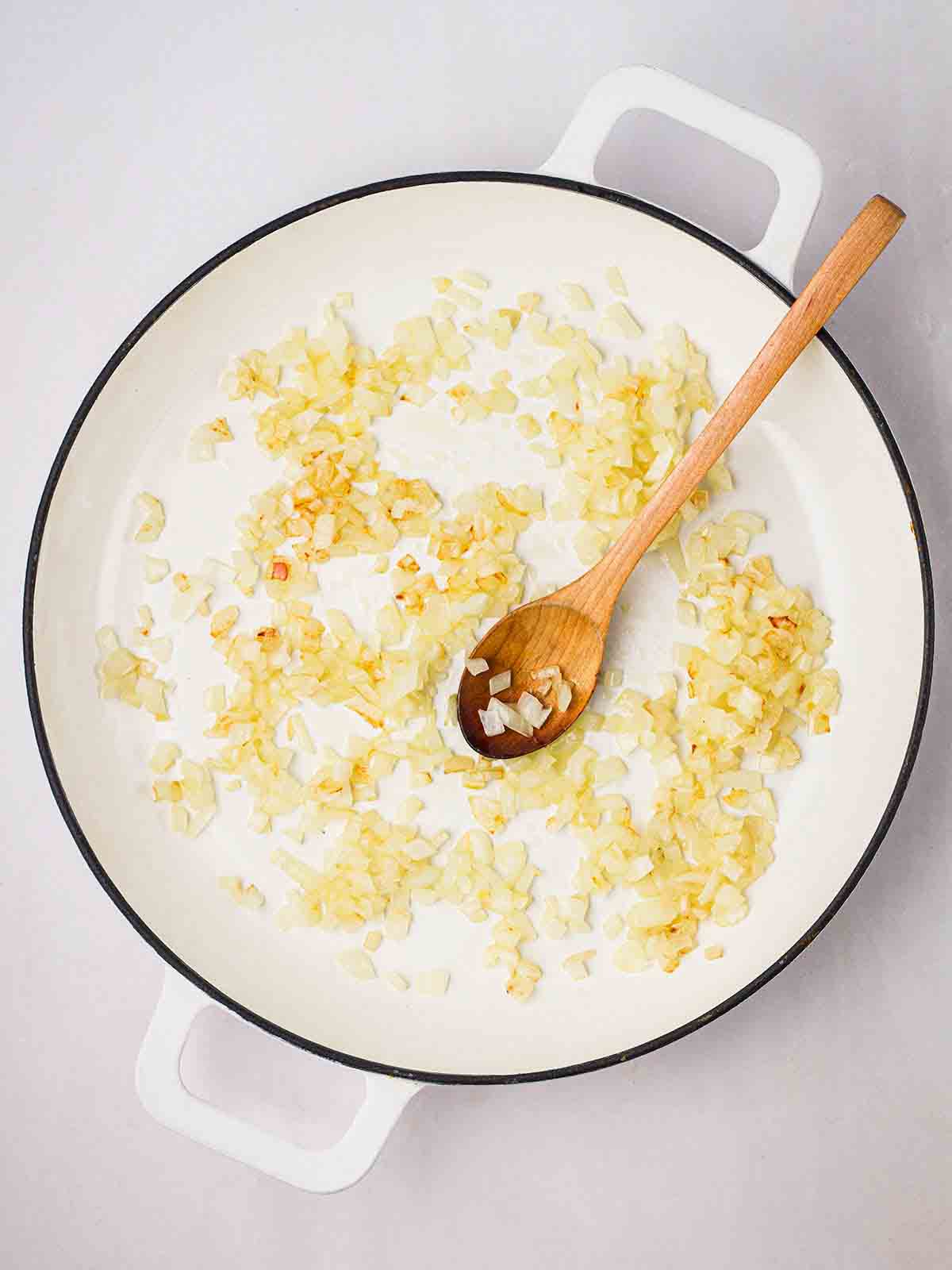 A pan filled with onions browning in oil and a wooden spoon to stir.