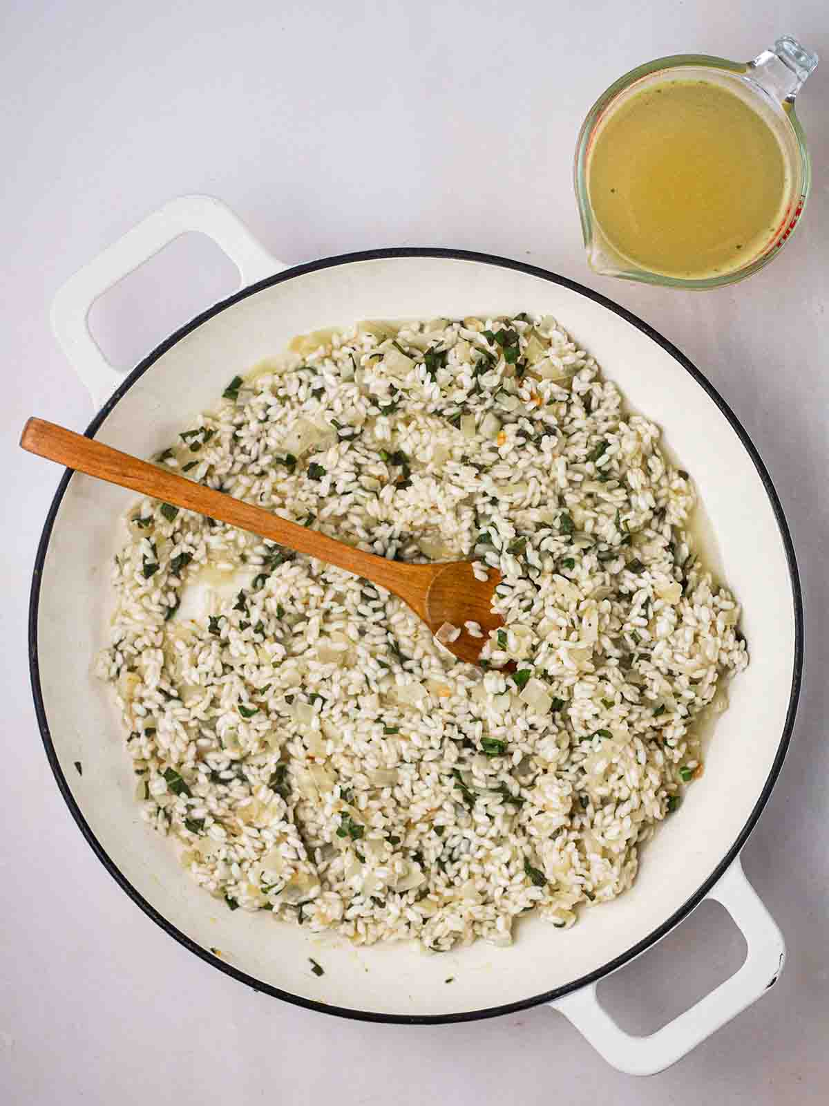 A risotto in a pan being cooked, with a jug of stock to the side.