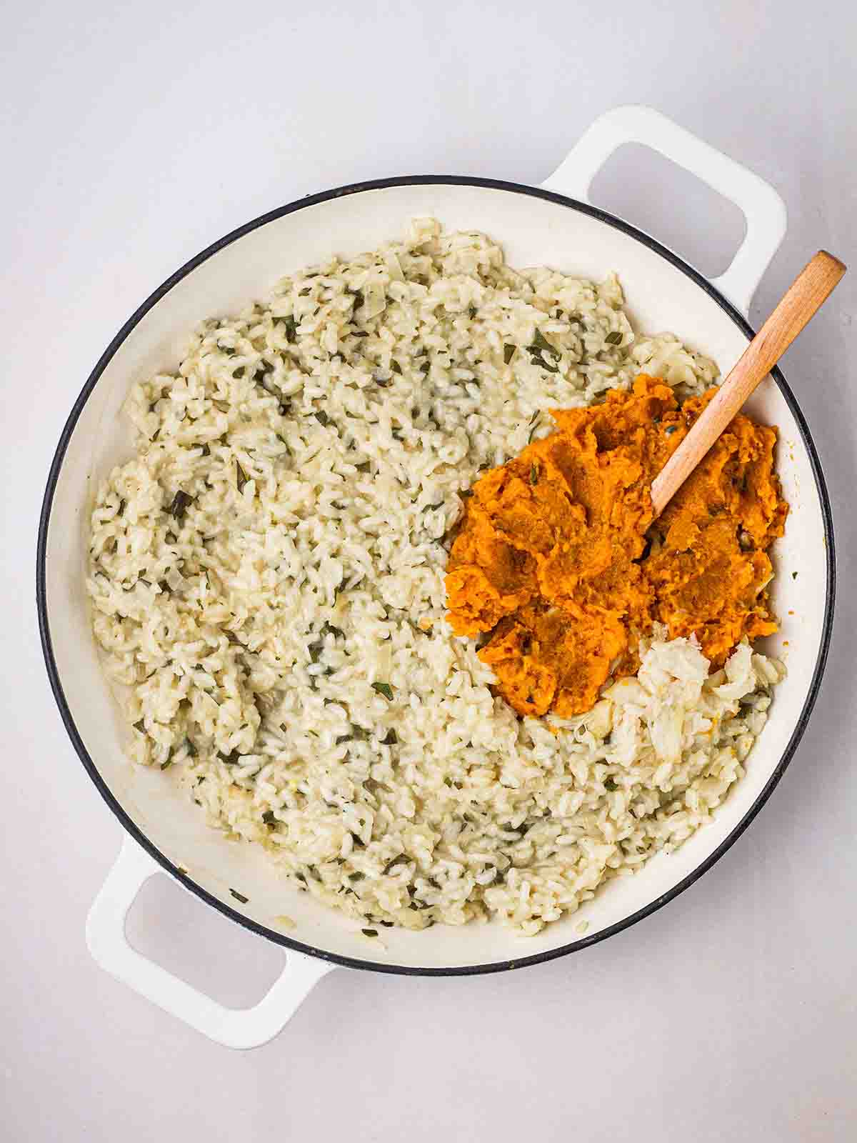 A pan filled with cooking risotto, with butternut squash about to be stirred in.
