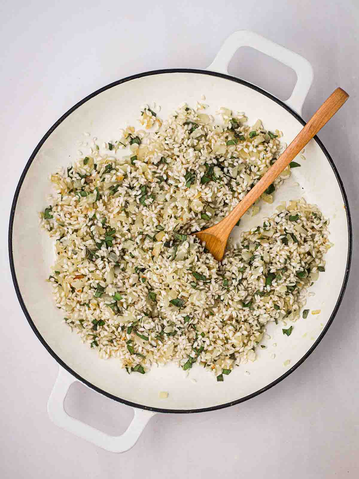 A pan with cooking risotto rice, sage and and onion, with a wooden spoon stirring.