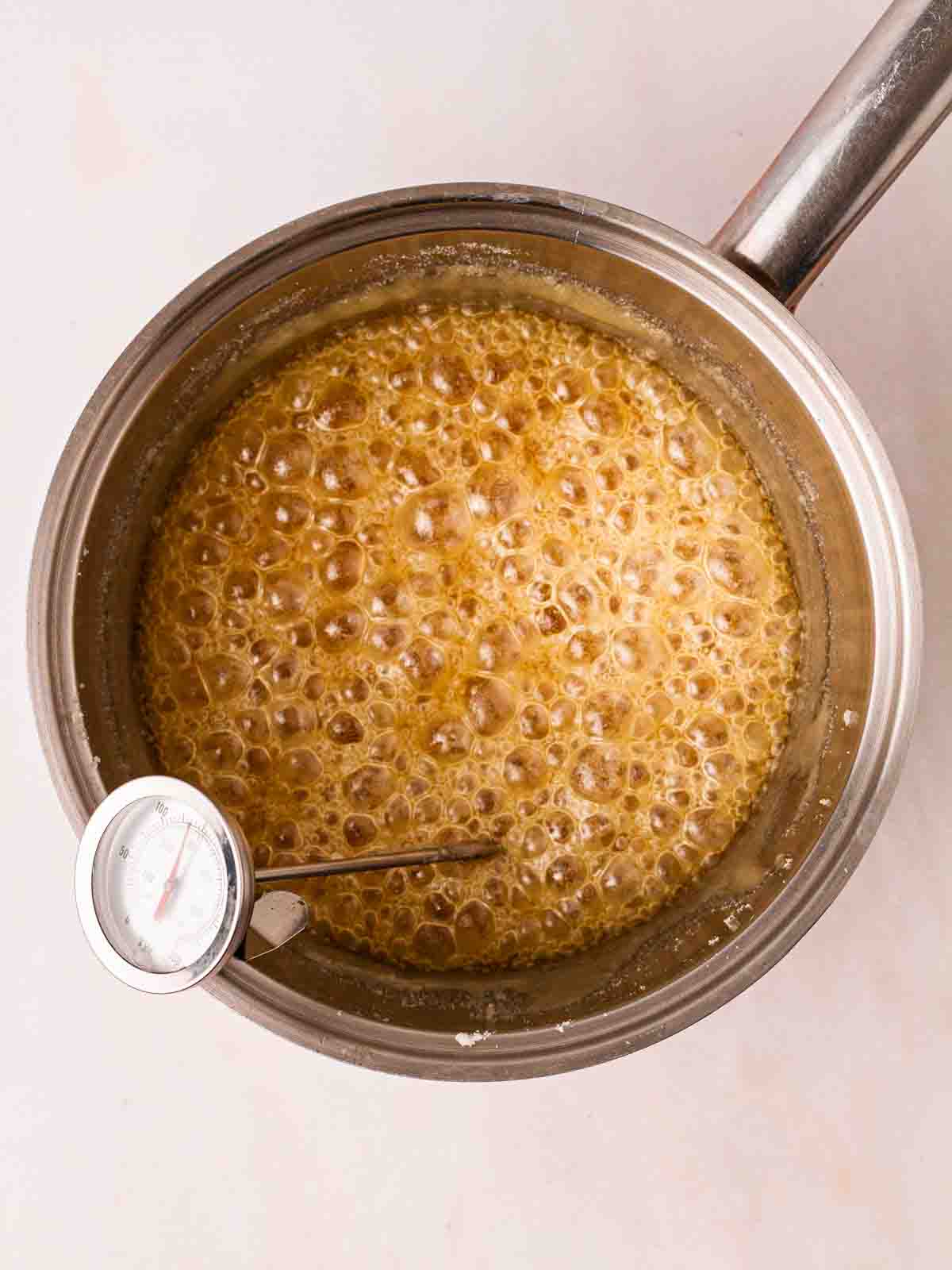 A thermometer in a pan of bubbling honeycomb for step 2 in the recipe process.