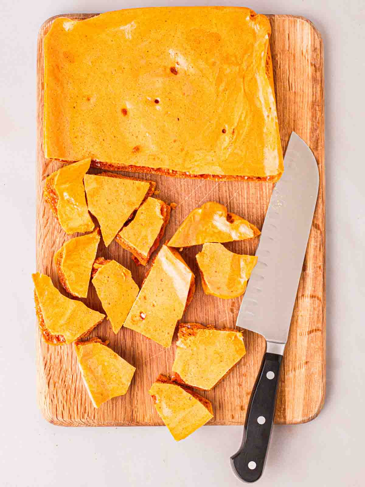 A wooden board with freshly homemade honeycomb on, with half cut into pieces with a knife.