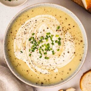 A bow of leek and potato soup with chives and black pepper on top, ready to eat.