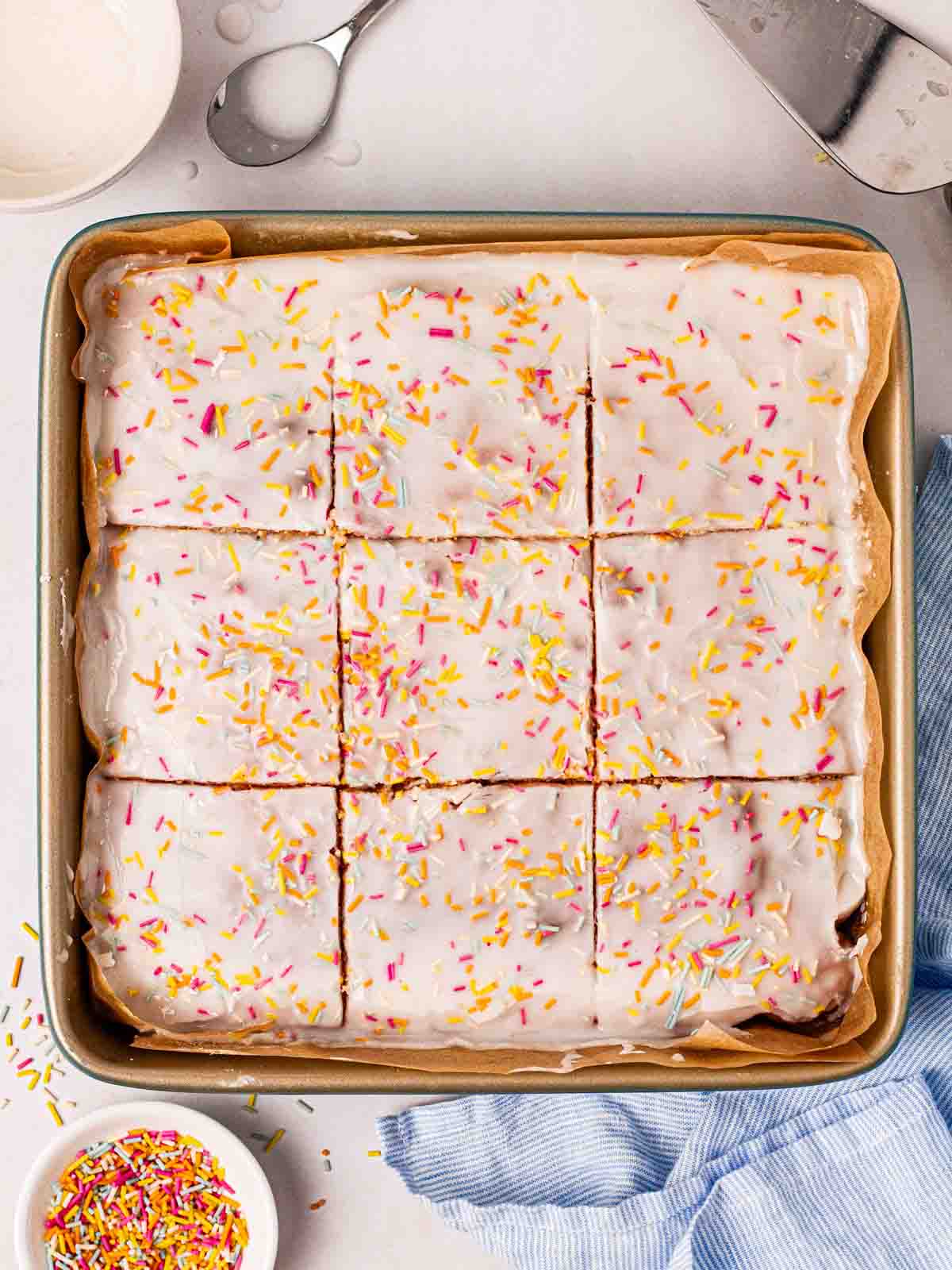 A square tin filled with a simple School Cake on a table with sprinkles over the top.