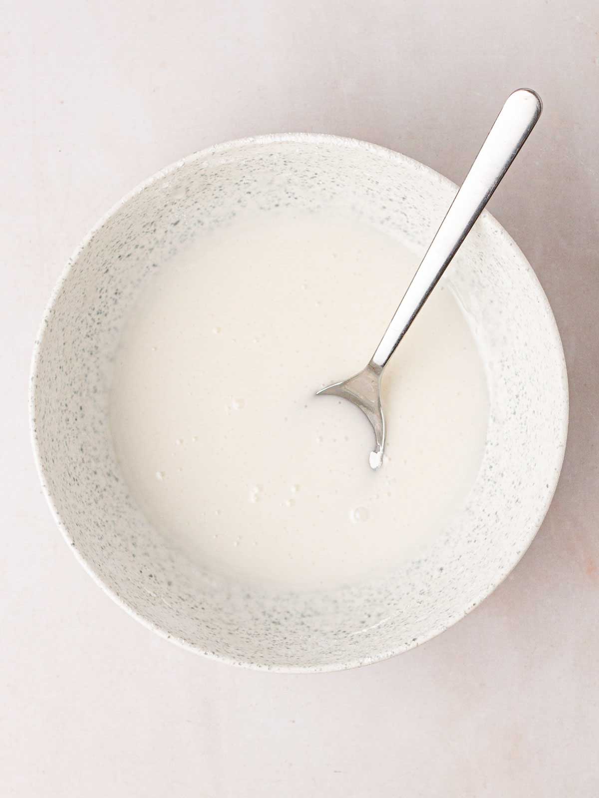 White icing in a bowl with a spoon inside.