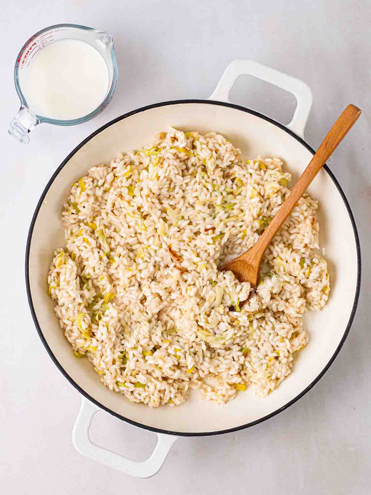 Risotto rice in a pan with a wooden spoon, with milk to the side, for step 2 in the recipe for Smoked Haddock Risotto.