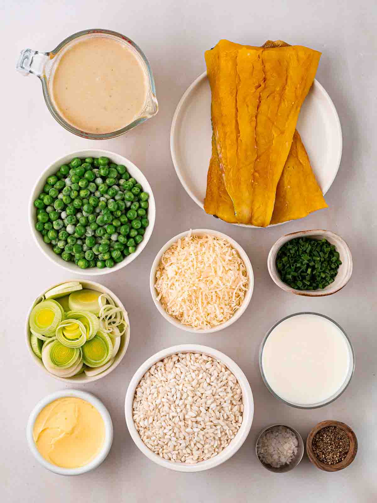 The ingredients for making Smoked Haddock Risotto laid out in bowls over a white surface.