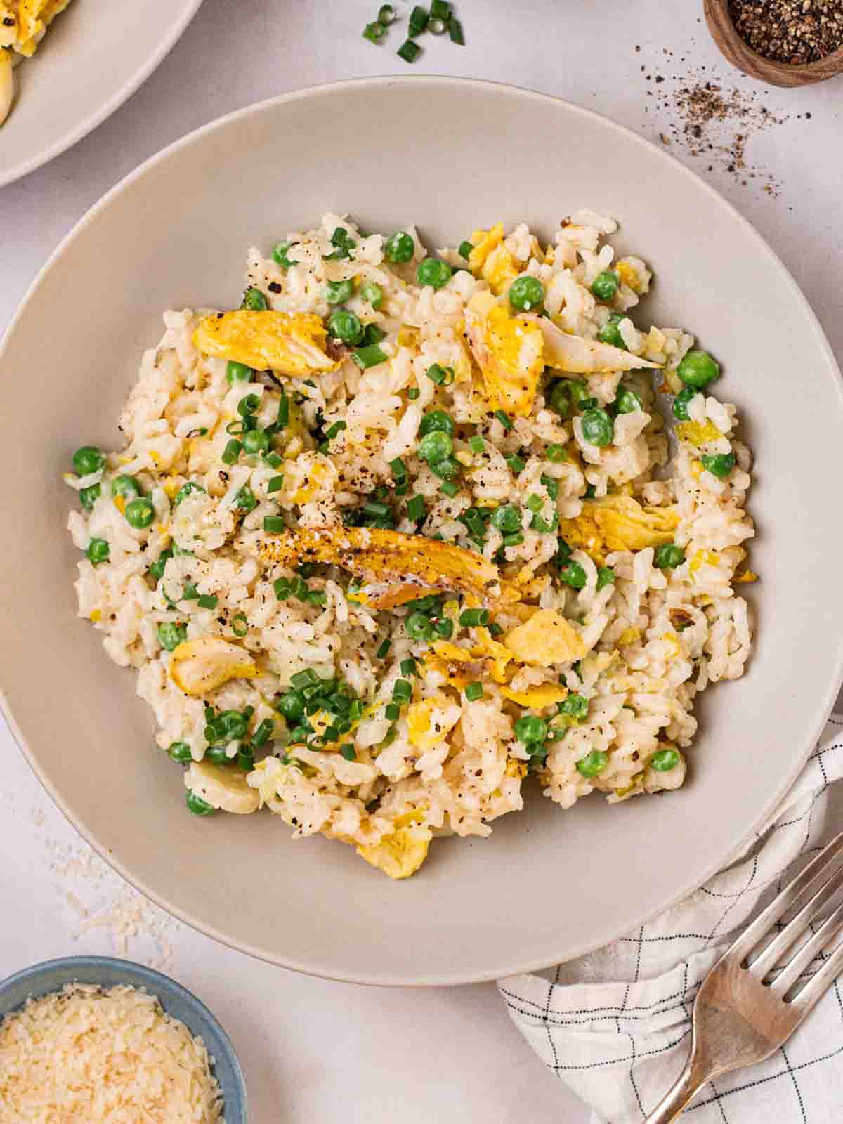 A white bowl filled with cooked Smoked Haddock Risotto, ready to eat with a fork at the side.
