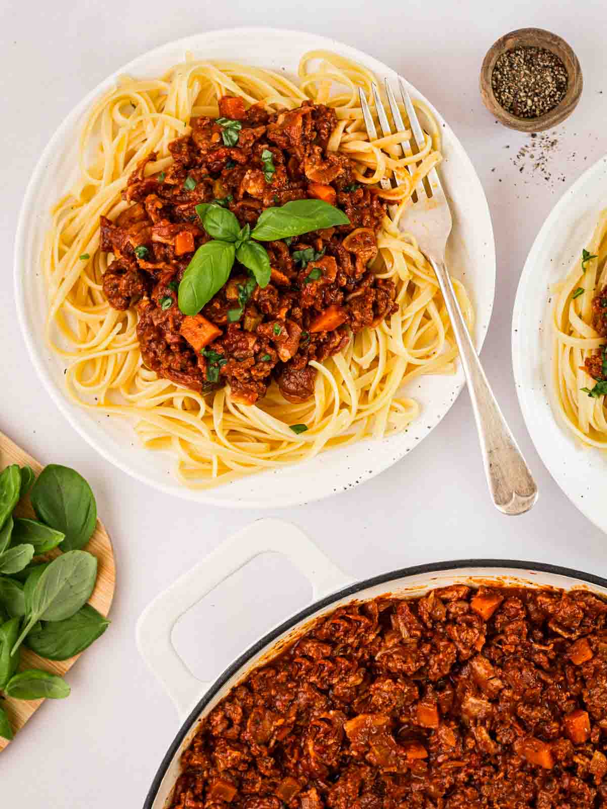 A plate of spaghetti bolognese with a large pan to the side to serve.