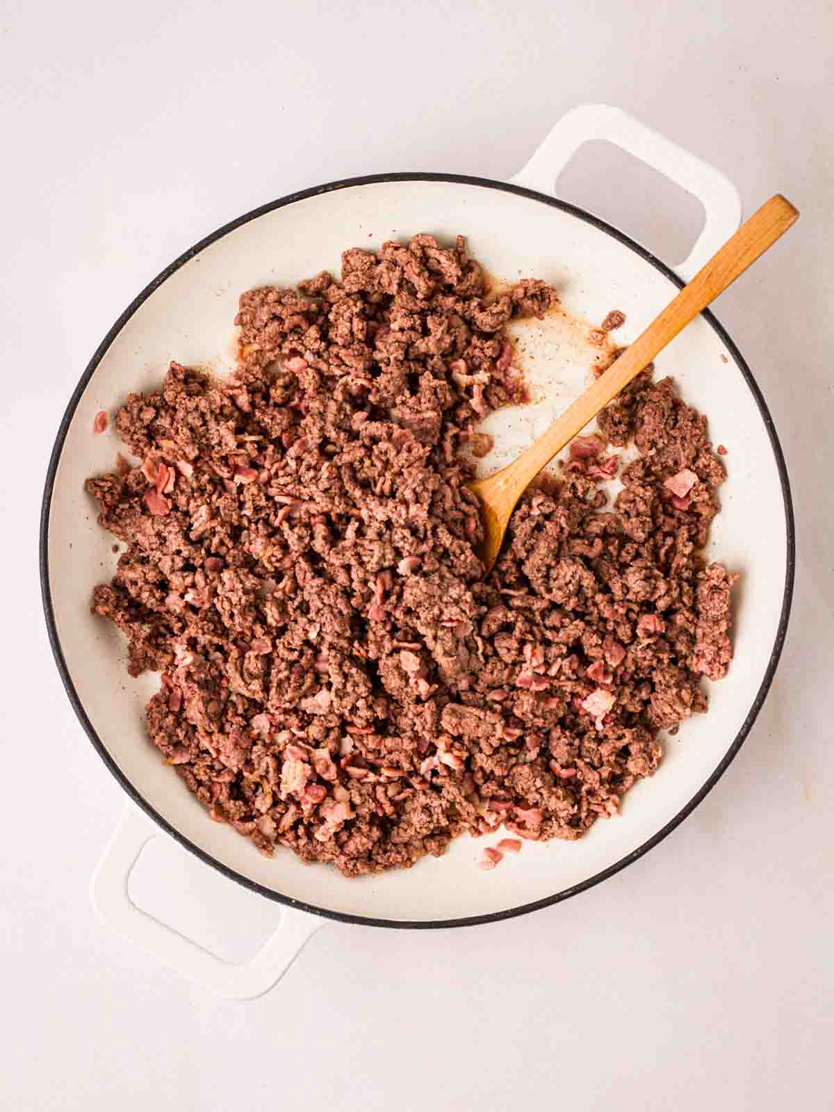 Mince frying in a white pan with a wooden stirring spoon in for step 2 in the recipe for Spaghetti Bolognese.