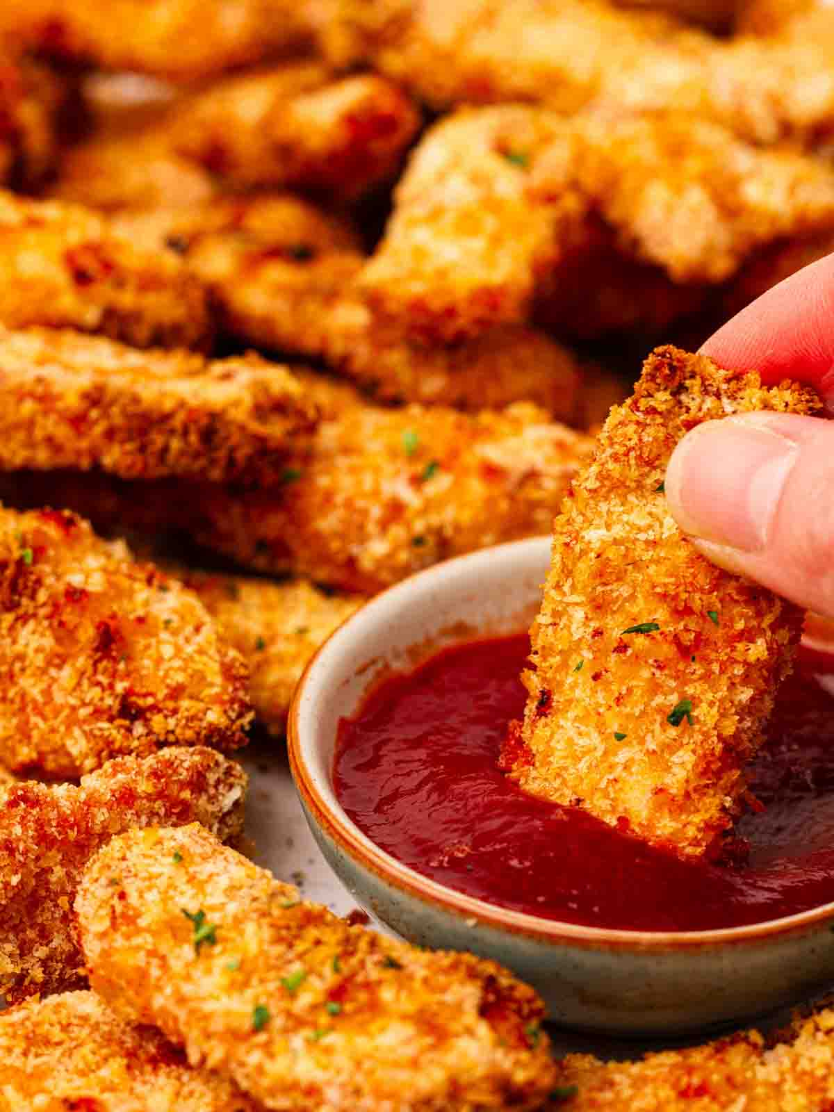 A plate of chicken goujons, with a hand dipping one into a bowl of ketchup.