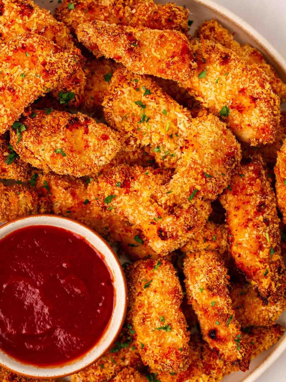 A plate filled with baked golden Chicken Goujons, with a bowl of ketchup to the side.