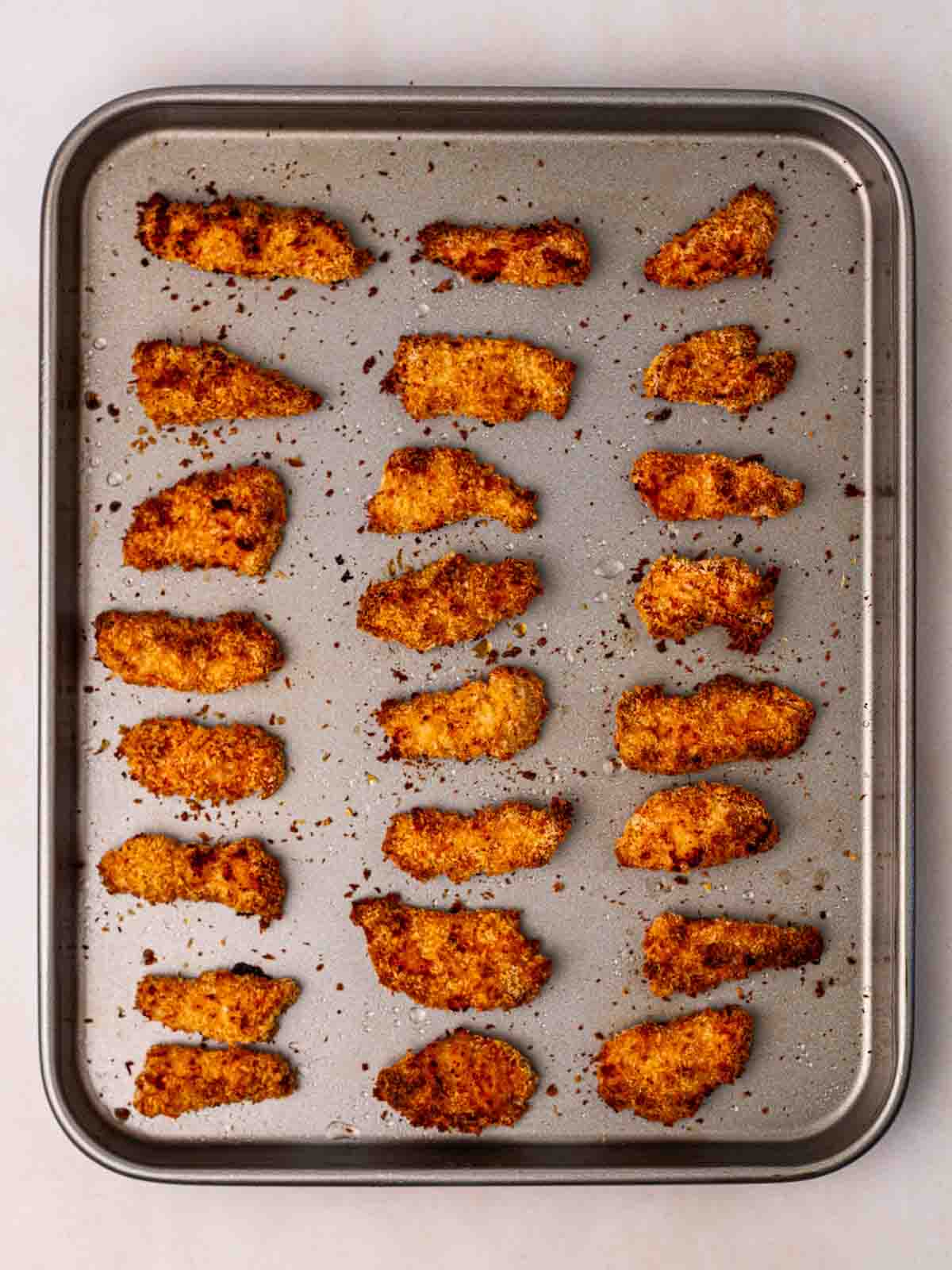 Rows of baked chicken goujons on a baking tray, just out of the oven.