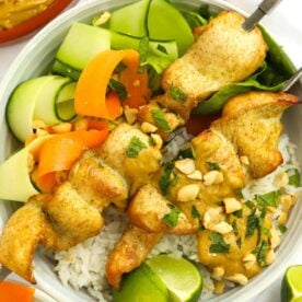 A bowl of chicken satay skewers with a side salad and rice, with peanuts over the top.