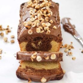 A Nutella Cake swirl loaf tin treat from the side, sliced, with hazelnuts on top.