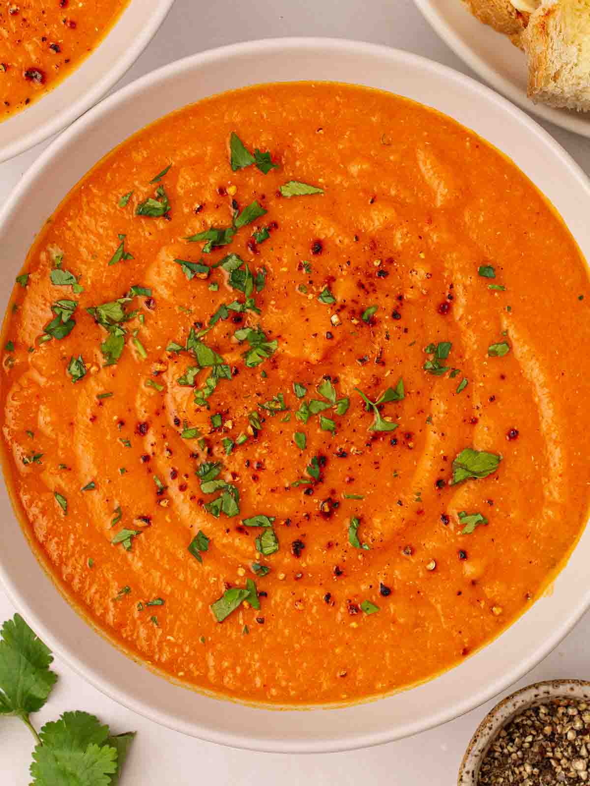 A bowl of orange Carrot and Lentil Soup with parsley sprinkled and cracked black pepper.