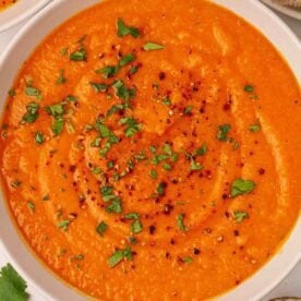 A bowl of thick spiced carrot and lentil soup, with a garnish of parsley and black pepper.