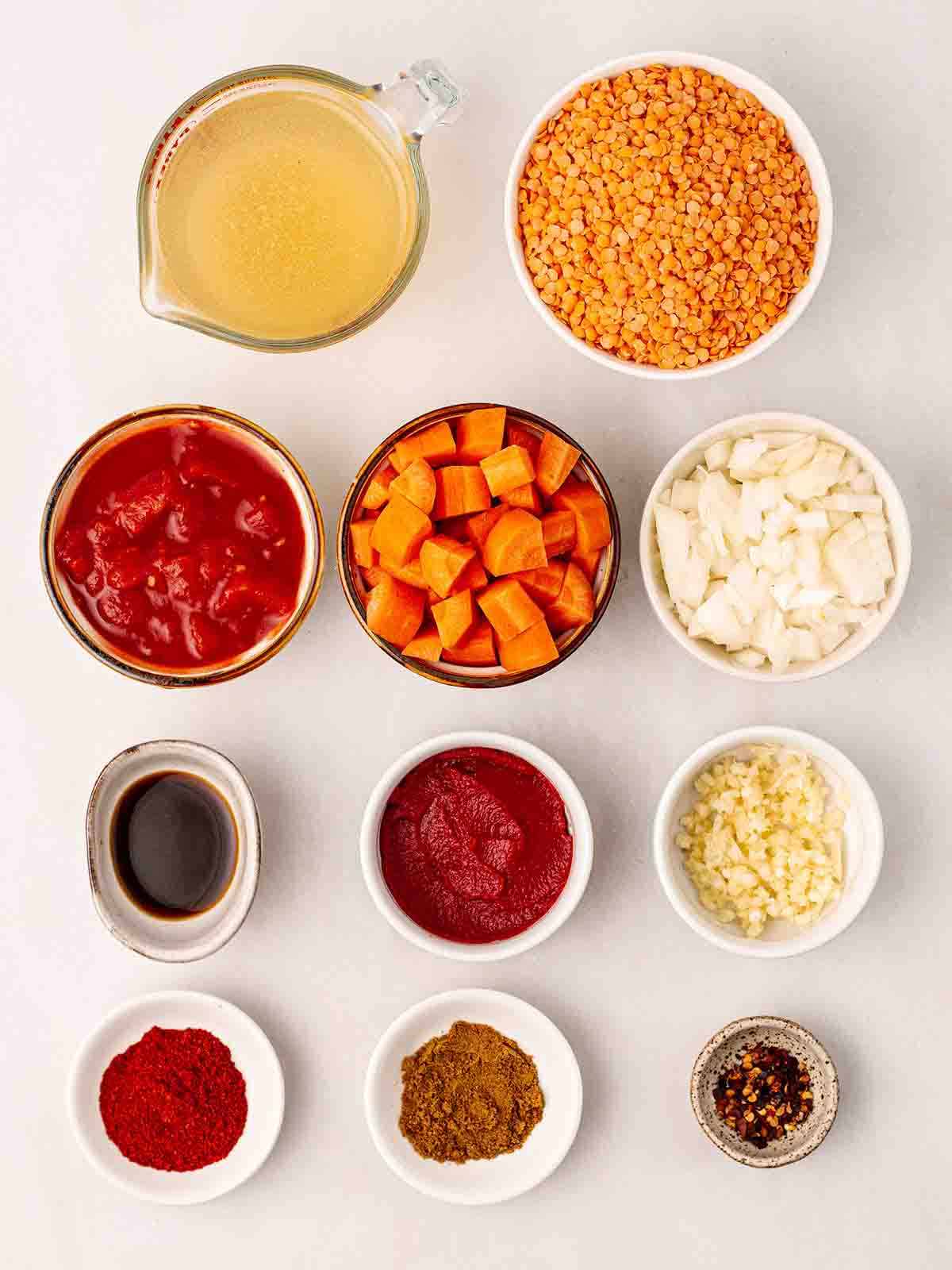 Ingredients for carrot and red lentil soup laid out in bowls on a white counter.