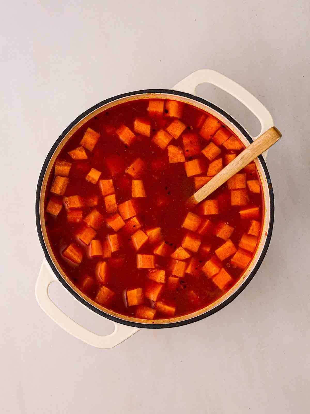 A pan of tomatoey liquid with chunks of carrot in for step 2 in the recipe for Carrot and Lentil Soup.