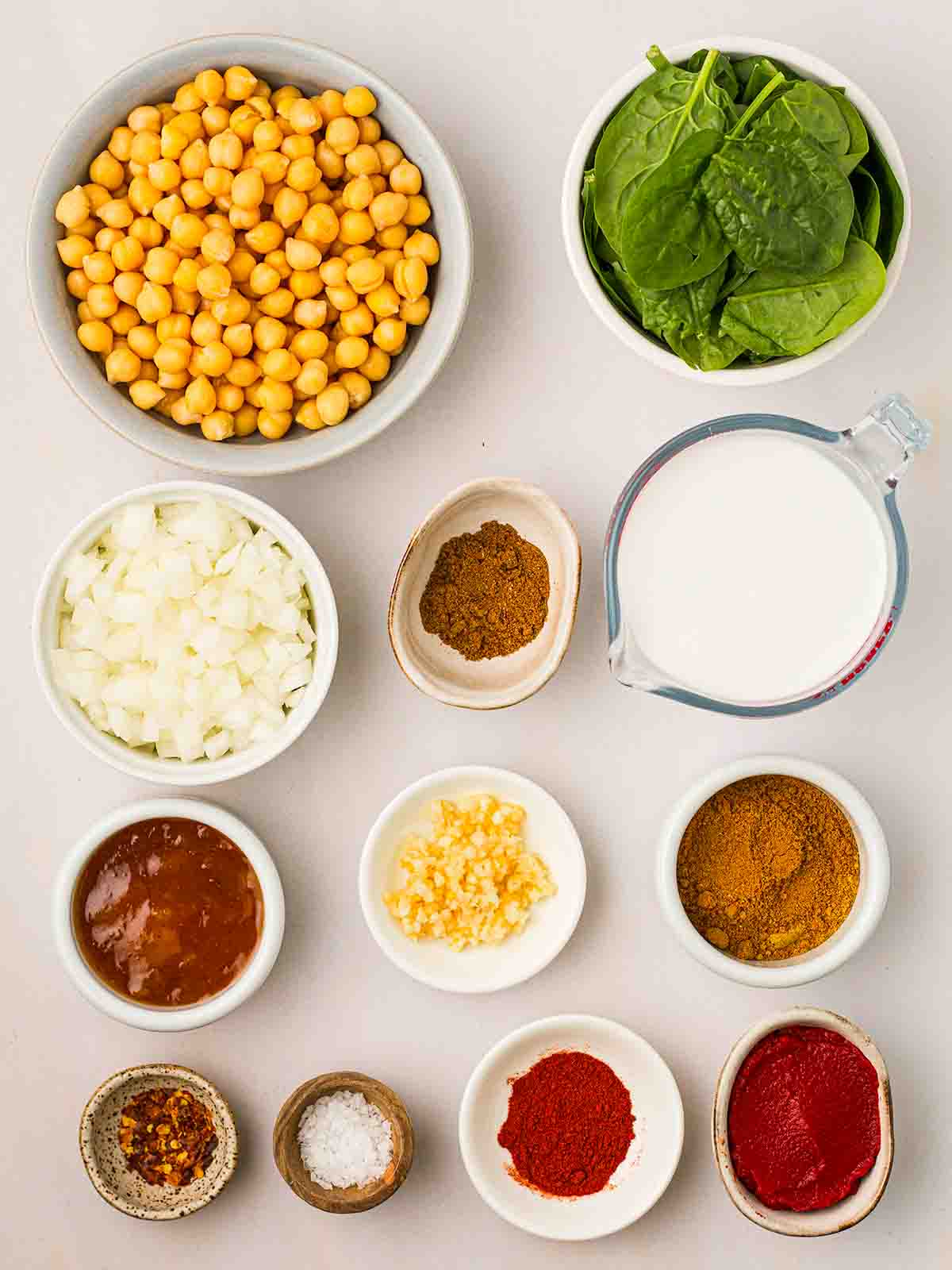 The ingredients for making Chickpea Curry laid out in small white bowls on a white surface.